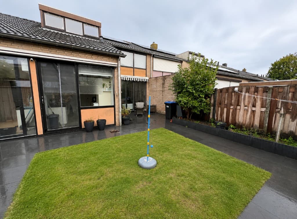 Originele achtertuin vóór de renovatie, met grasveld, tegelterras en beplanting langs de woning.
