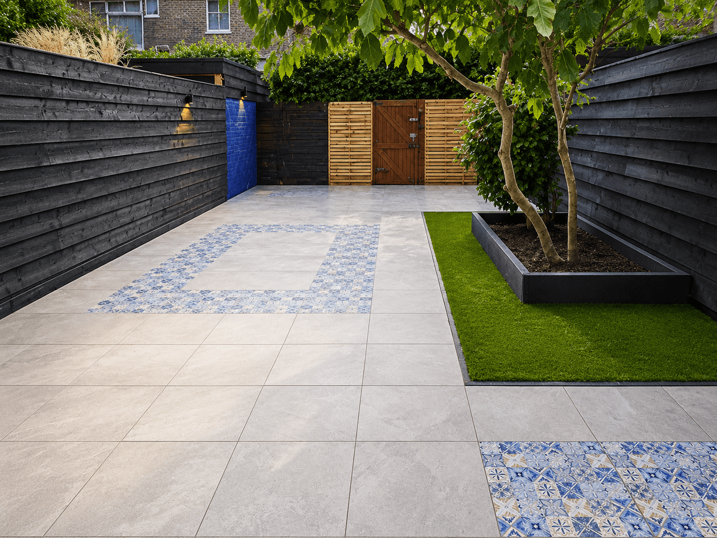 Afgewerkte tuin met lichte bestrating, decoratieve accenttegels, verhoogde plantenbak en een kunstgrasstrook.