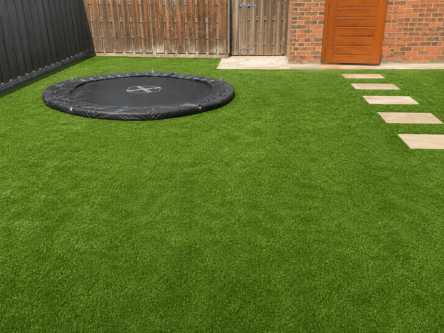 Kindvriendelijke achtertuin na de renovatie, met kunstgras en een verzonken trampoline.