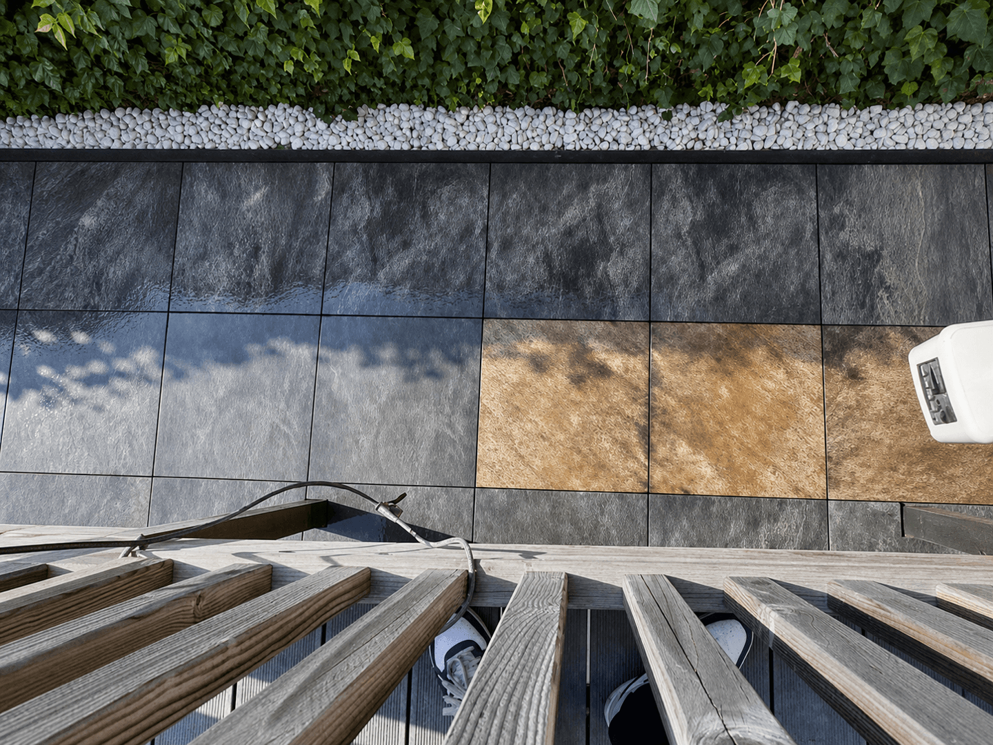 Afgewerkte zithoek in de tuin, van boven gezien, met nieuwe wandtegels, grindstrook en loungeset.