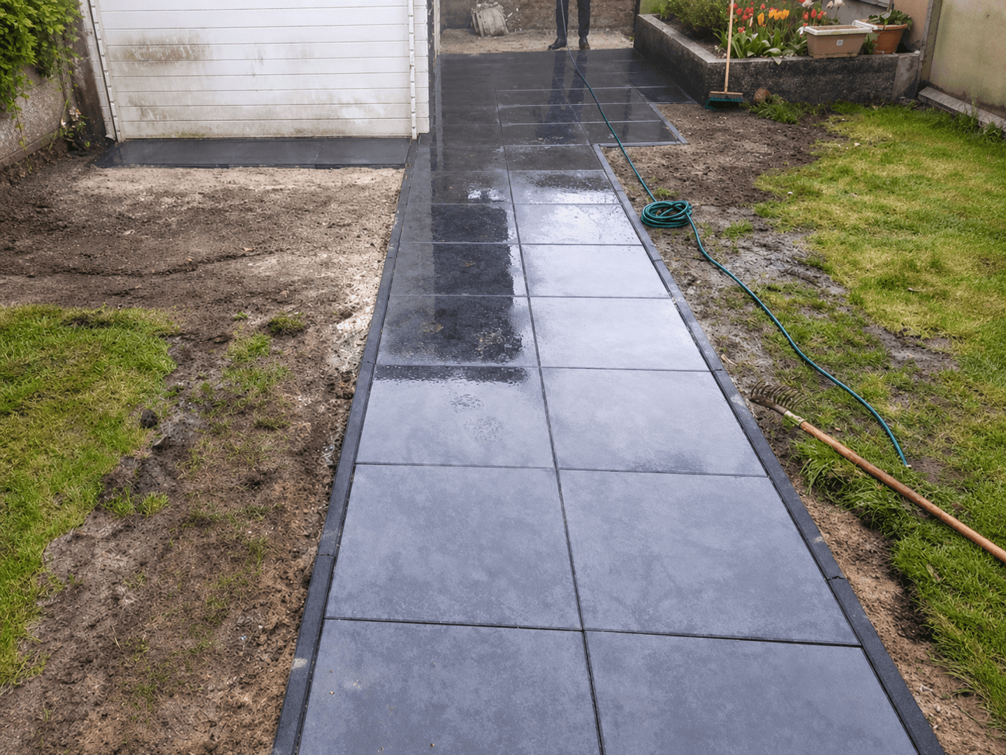 Nieuw looppad van grote antracietkleurige tegels met strakke opsluitbanden door de tuin.