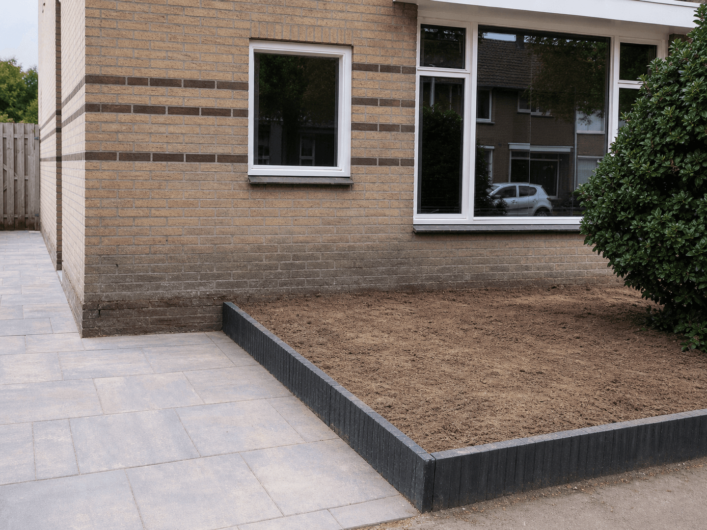 Vernieuwde tuin met keramische bestrating en een verhoogde border, klaar voor beplanting.