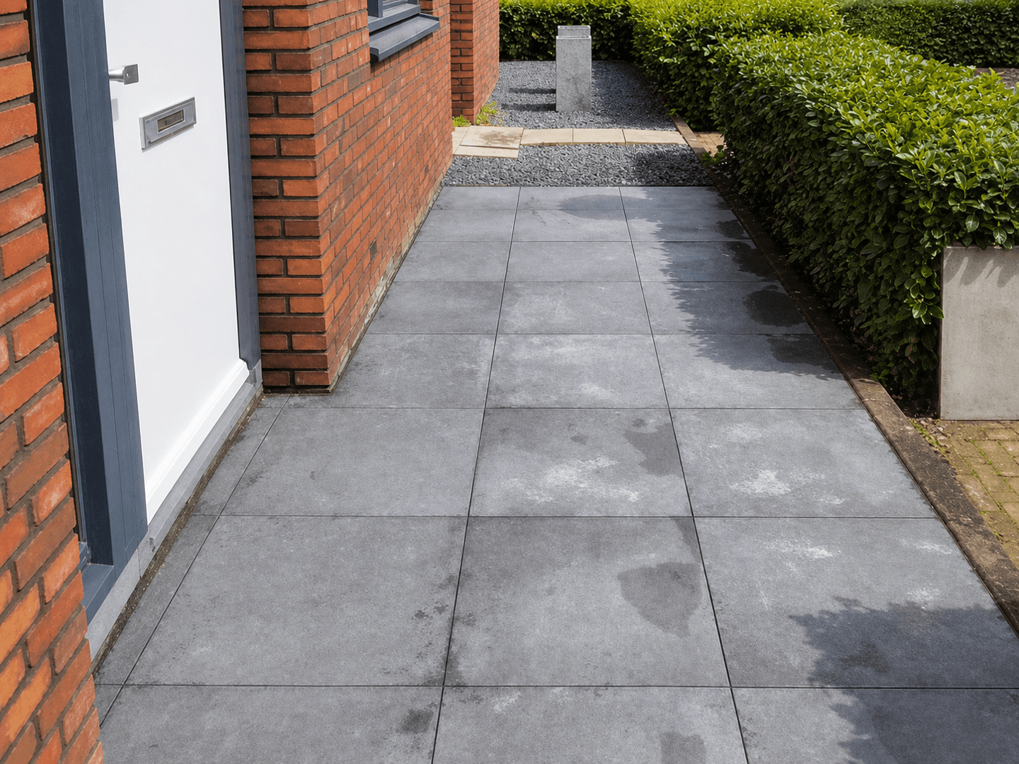 Nieuw bestraat zijpad langs de woning, met grote grijze tegels en een strakke haagrand.