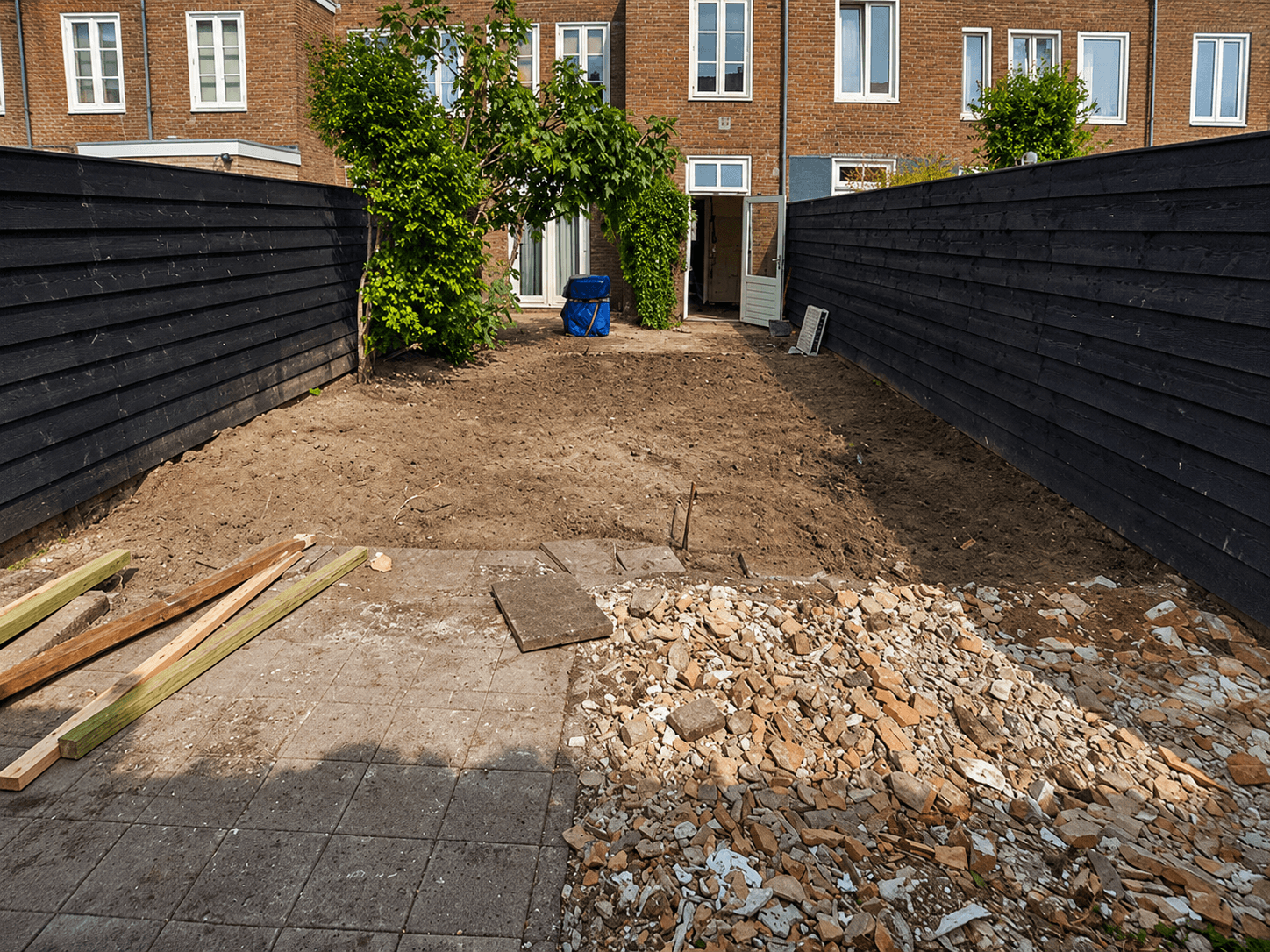 Stadstuin vóór de renovatie, met kale grond, puin en opgebroken bestrating.