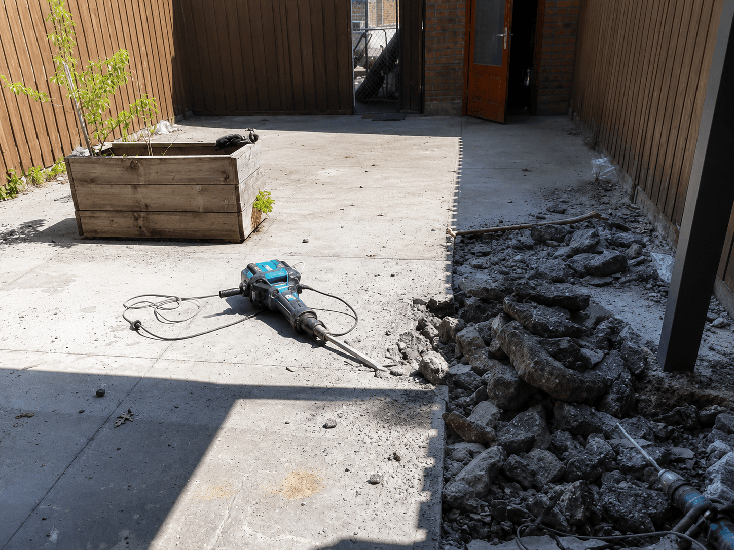 Opbreken van de oude betonnen ondergrond in de achtertuin tijdens de sloopfase.