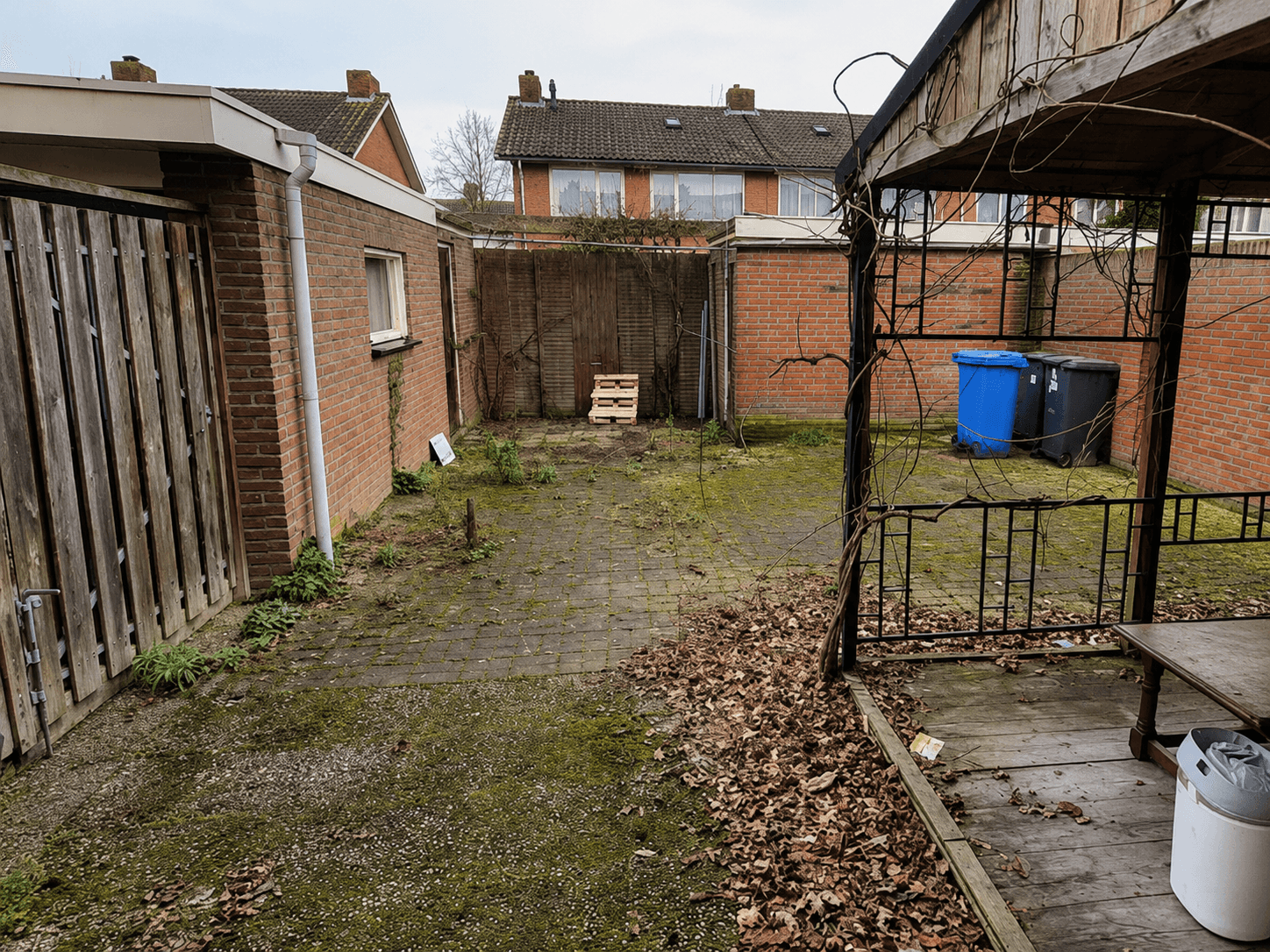 Verwaarloosde achtertuin met mos, bladafval en oude tegels vóór de renovatie.