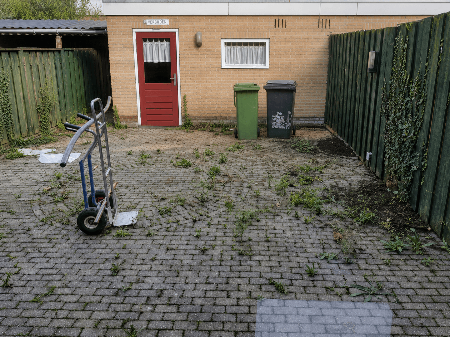 Oude gebakken klinkers met onkruid en verzakkingen vóór de nieuwe bestrating.