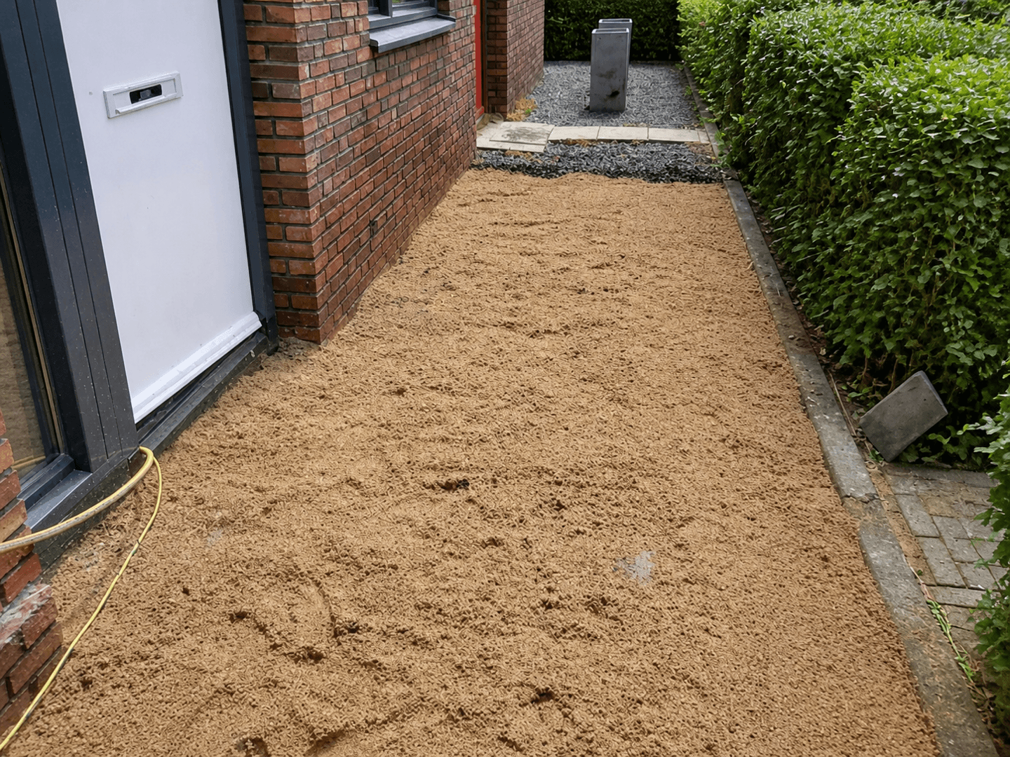 Zijpad langs de woning uitgevlakt met straatzand, klaar voor de nieuwe tegels.